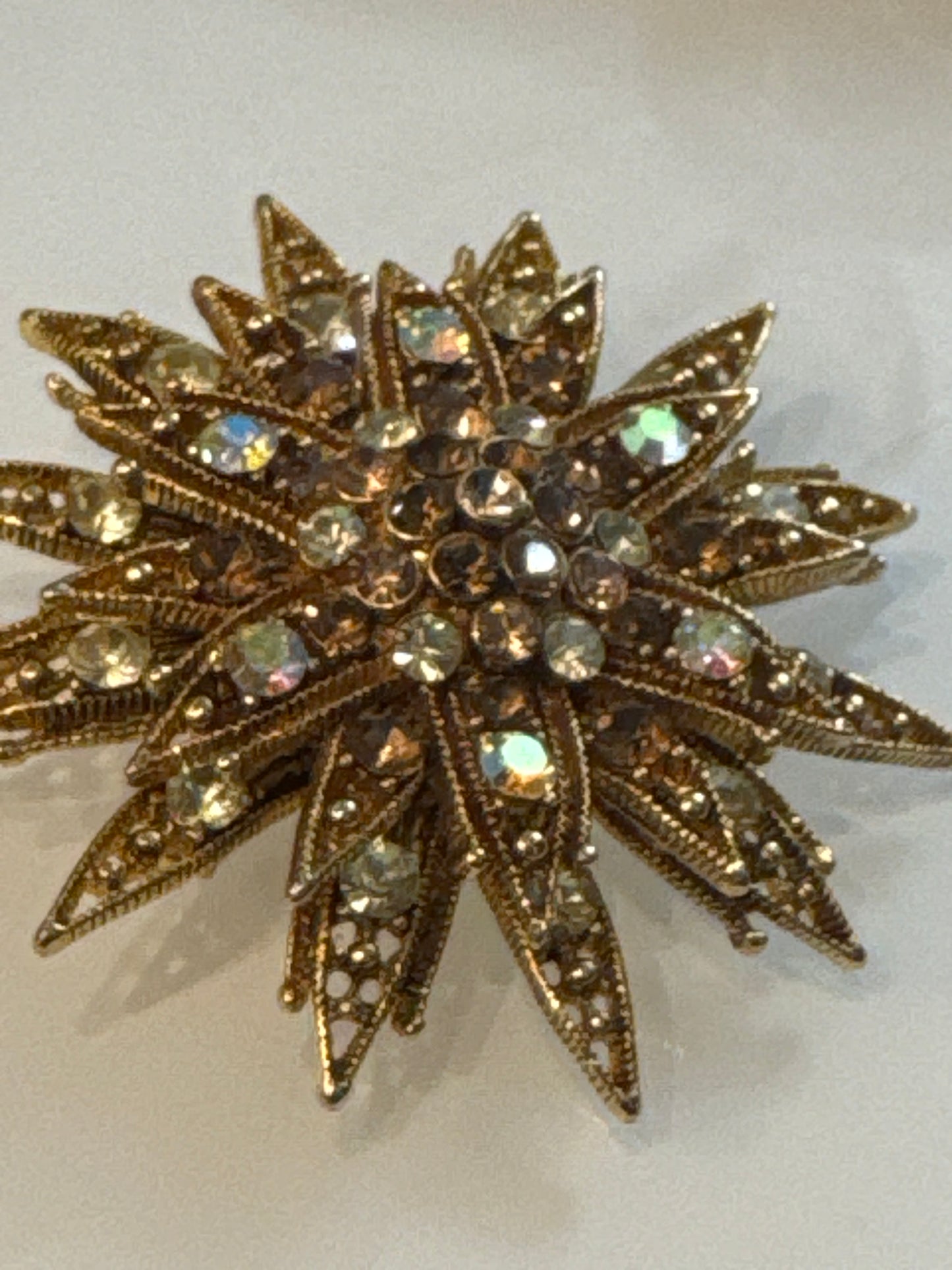 Mid-century rhinestone starburst brooch, c. 1950s–60s, featuring smoky topaz and aurora borealis crystals in sculptural gold-tone metal.