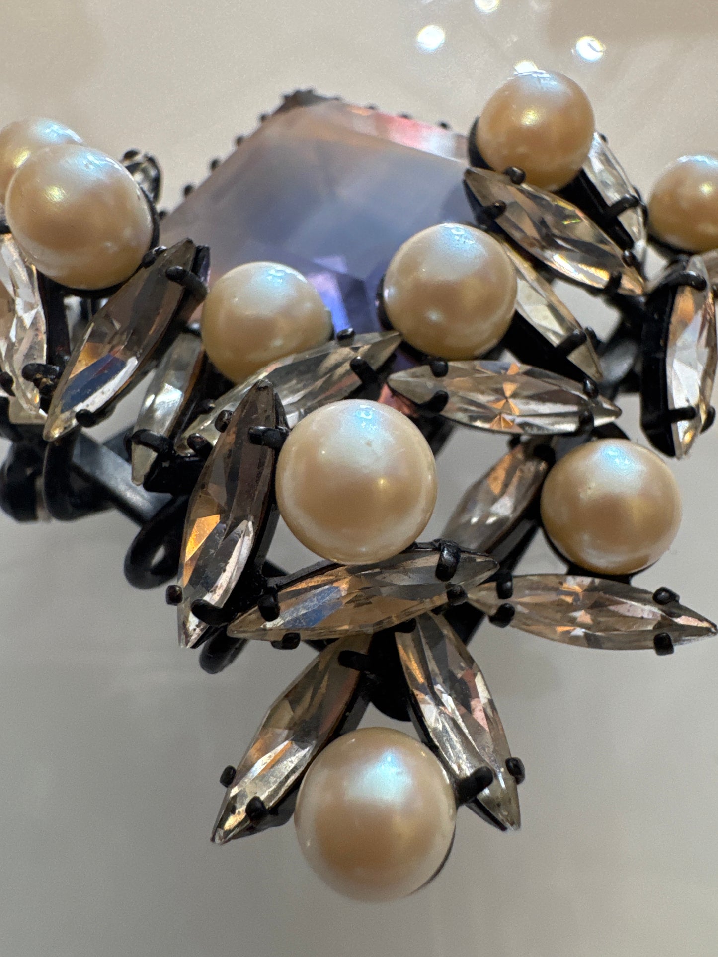 Sculptural mid-century couture brooch featuring a faceted lavender glass center stone, framed by faux pearls and clear navette rhinestones in black japanned metal. Atelier-made, circa 1950s–60s. Architectural, dramatic, and exquisitely constructed.