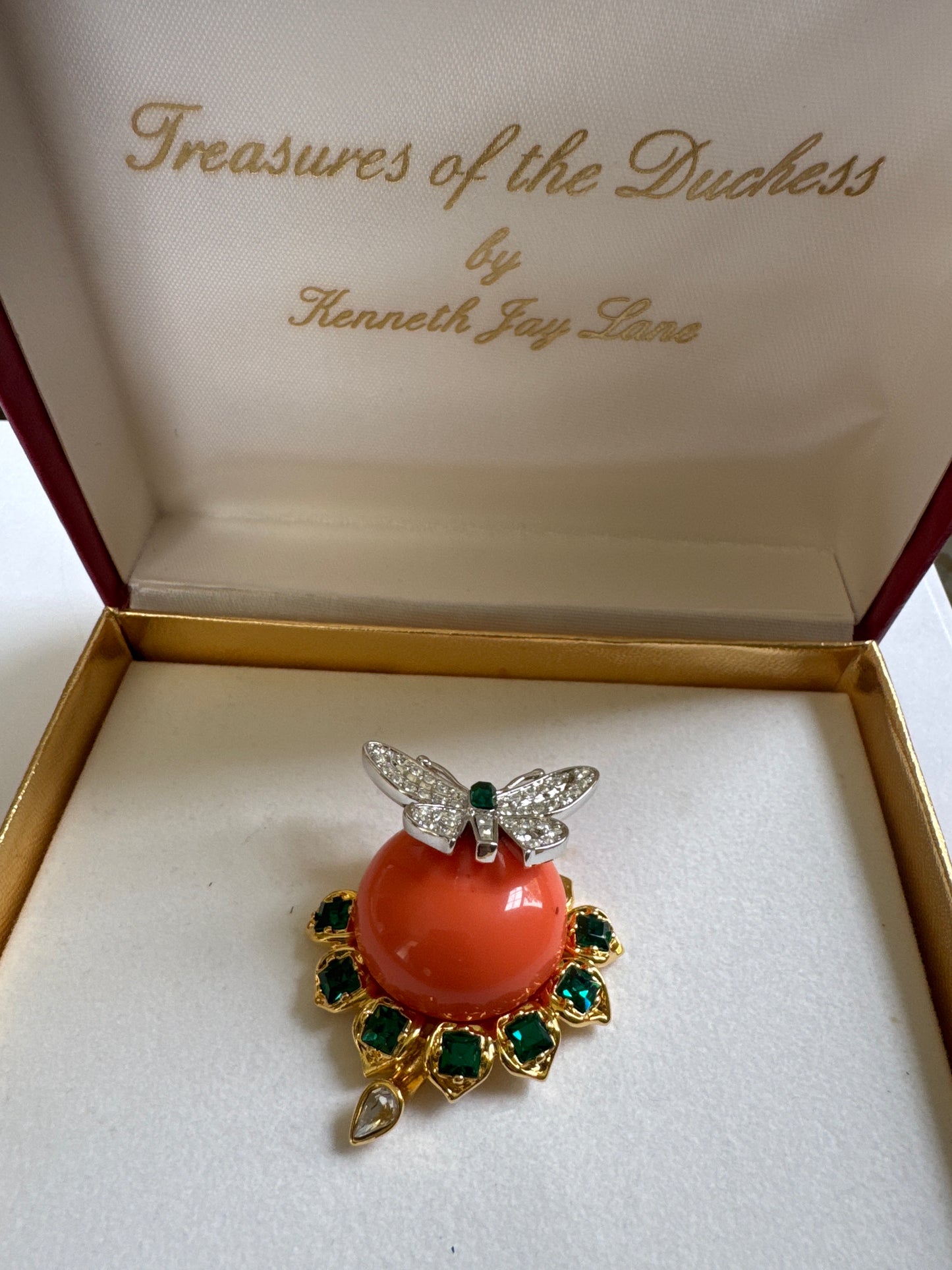 A boxed Kenneth Jay Lane ‘Treasures of the Duchess’ brooch, originally sold through QVC—featuring a coral-tone cabochon, emerald rhinestones & a whimsical dragonfly detail. Made by KJL after a piece from his friend, The Duchess of Windsor's own collection