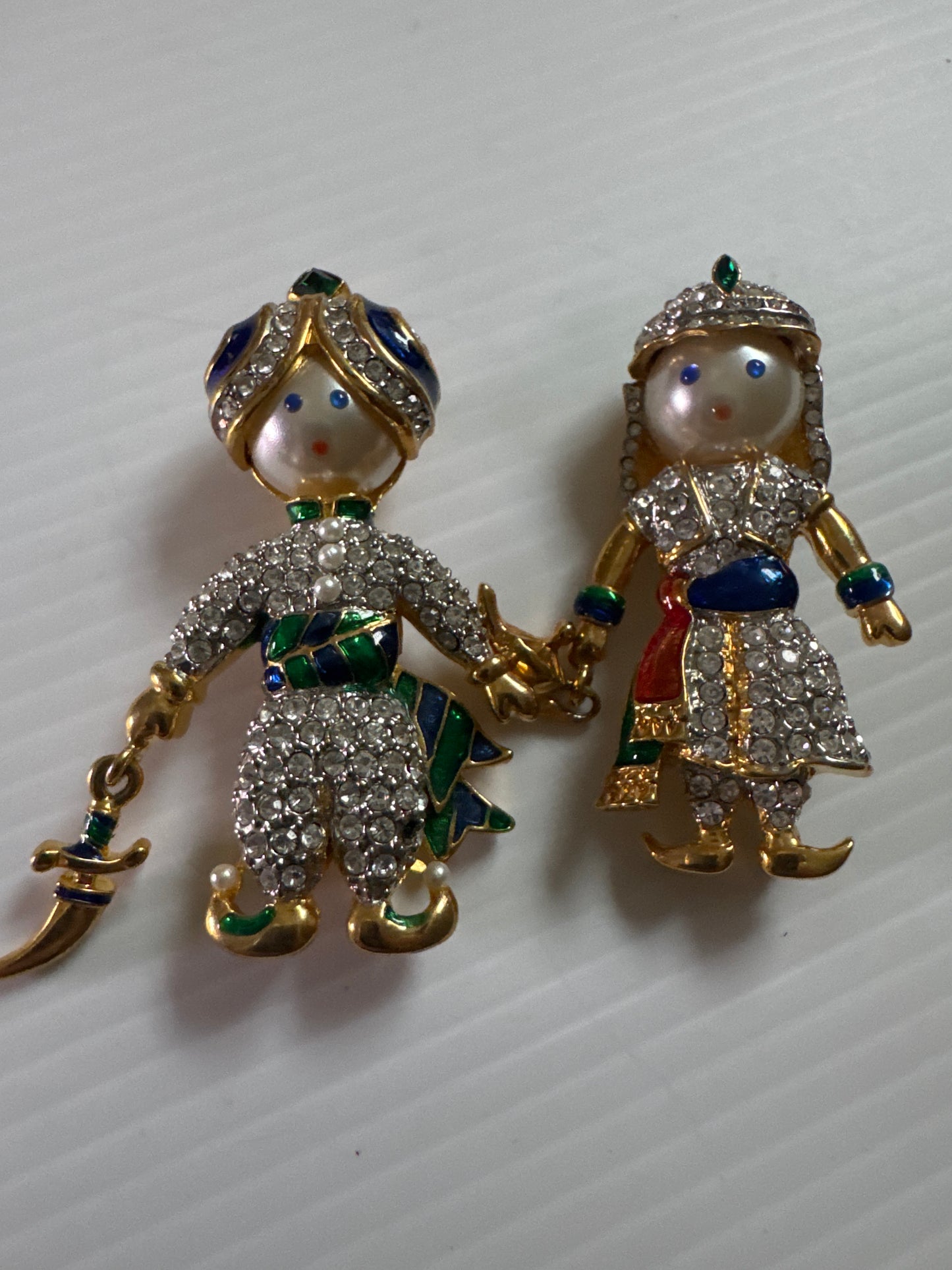 A whimsical 1980s vintage pair inspired by Arabian Nights fantasy—this figural duo features a genie and his companion, each richly detailed with hand-set rhinestones, enamel accents, and expressive pearlized faces.