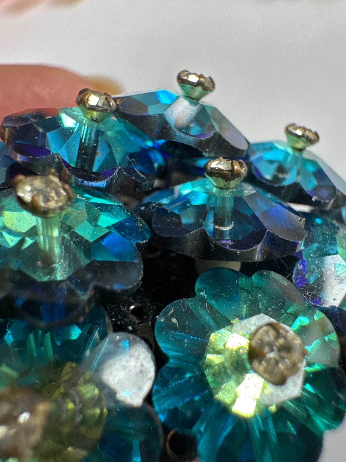 A striking vintage brooch composed of layered, faceted crystal florets in rich shades of teal, emerald, and deep ocean blue. Each petal-like stone is cut to catch the light from every angle, creating a dimensional, almost floral cluster effect that feels