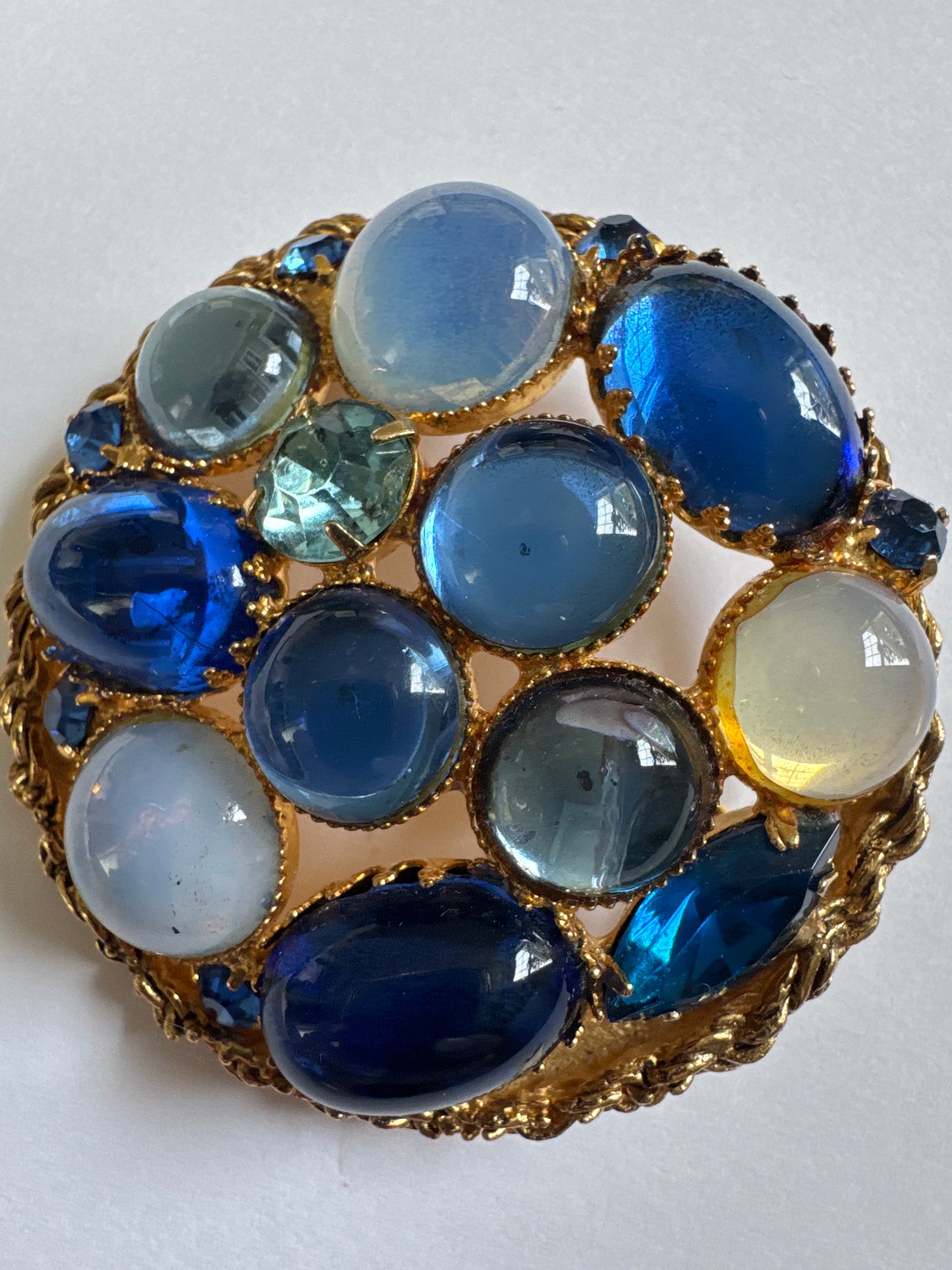 Gorgeous 1950s brooch featuring a mix of luminous blue Czech glass cabochons ranging from milky moonstone tones to deep sapphire hues, plus some cut rhinestones for additional depth