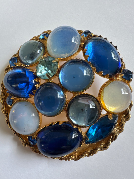 Gorgeous 1950s brooch featuring a mix of luminous blue Czech glass cabochons ranging from milky moonstone tones to deep sapphire hues, plus some cut rhinestones for additional depth