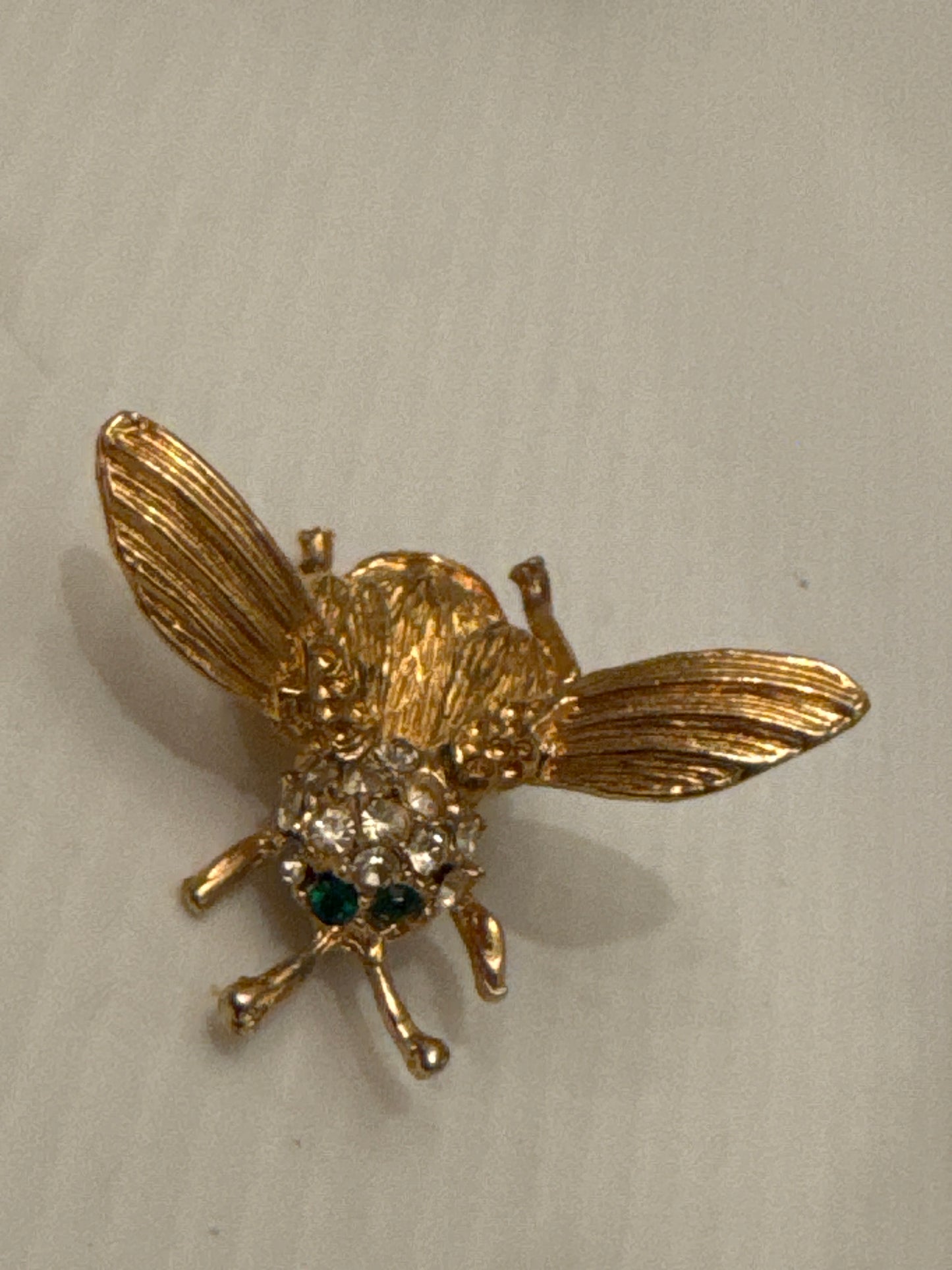 Unsigned vintage trembler brooch, attributed to Hattie Carnegie, circa late 1940s. Identified by its sculptural gold-tone body, ribbed wings, green crystal eyes, and classic Carnegie tremble construction.