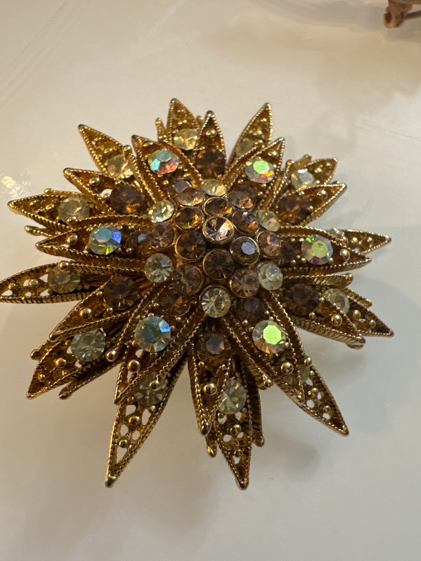 Mid-century rhinestone starburst brooch, c. 1950s–60s, featuring smoky topaz and aurora borealis crystals in sculptural gold-tone metal.