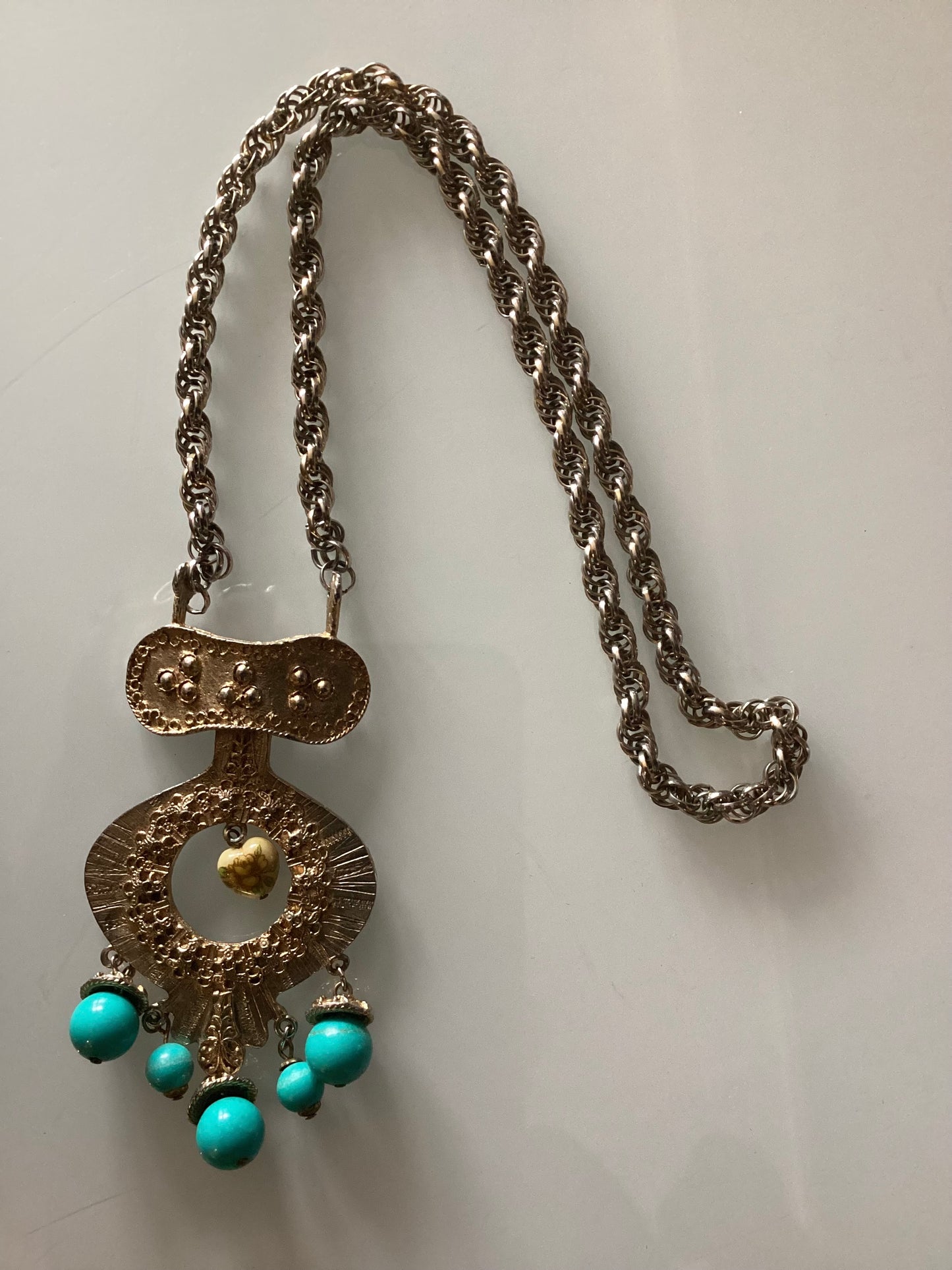 Pendant necklace with turquoise dangle and a small heart with flowers in the center