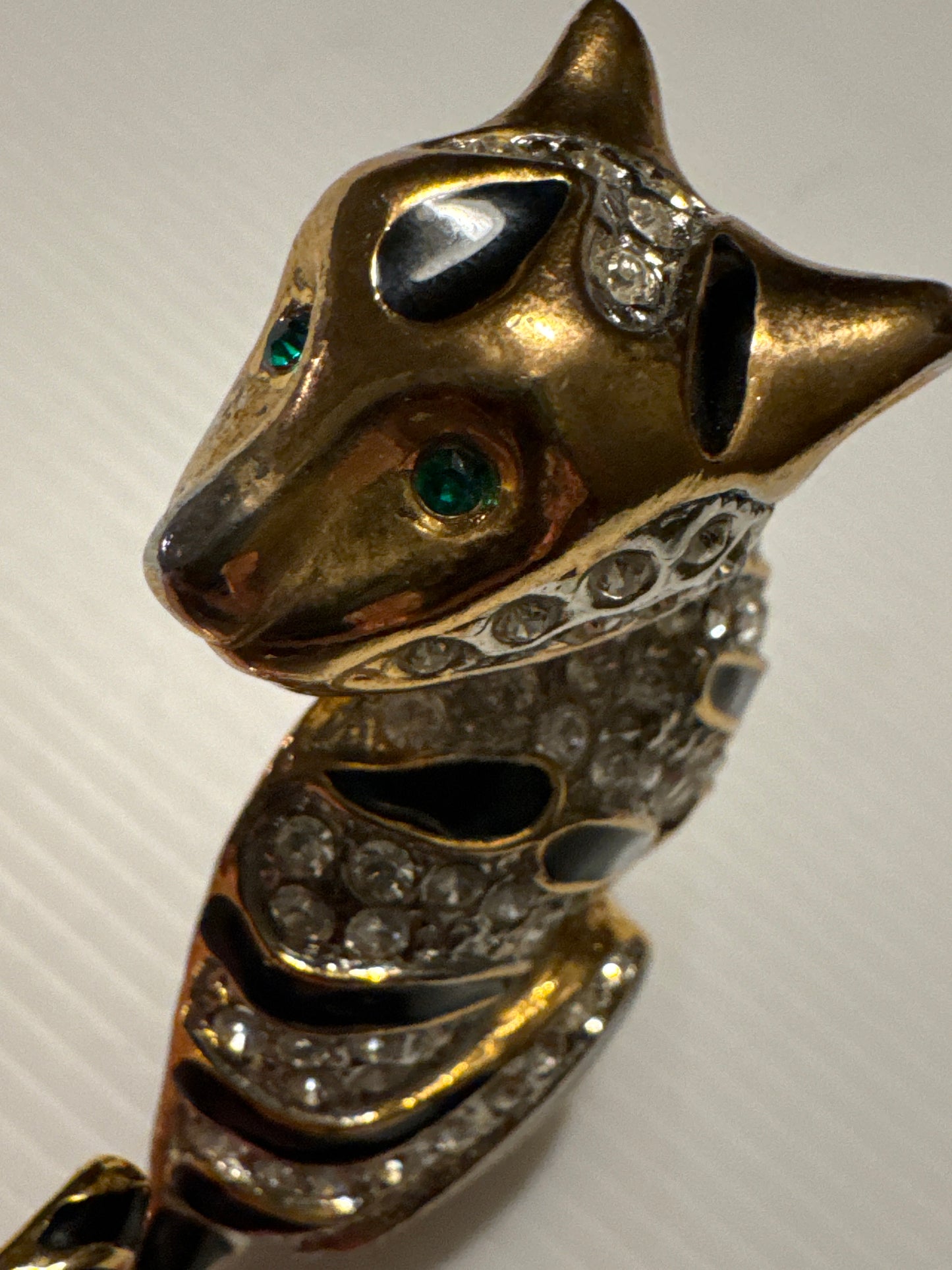 1980s jumbo gold tone, black enamel, and clear rhinestone cheetah brooch with green emerald eyes