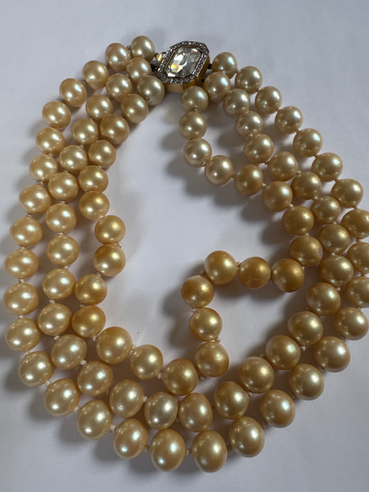 1980s vintage triple strand champagne colored hand-knot pearls by Kenneth Lane very similar to the ones Jackie Kennedy wore on the cover of LIFE magazine that made him famous! The clasp is a beautiful emerald cut clear stone surrounded by rhinestones.