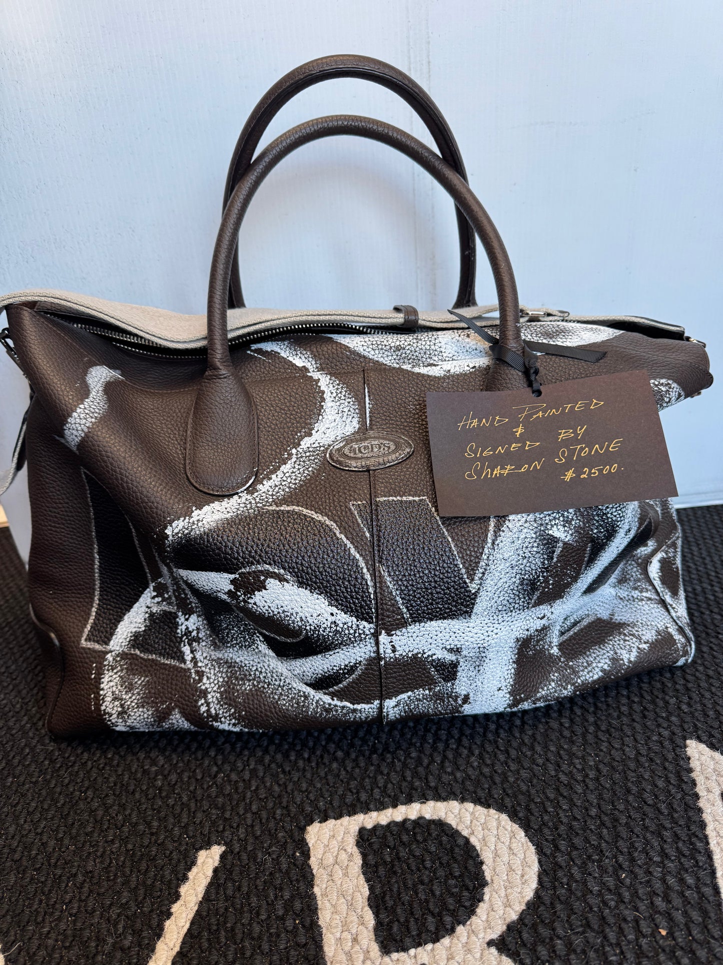 Hand-painted with "LOVE"and Signed by actress Sharon Stone this Tod's brown leather weekender looks as fab on the road as it does in your home a display housing cozy blankets.