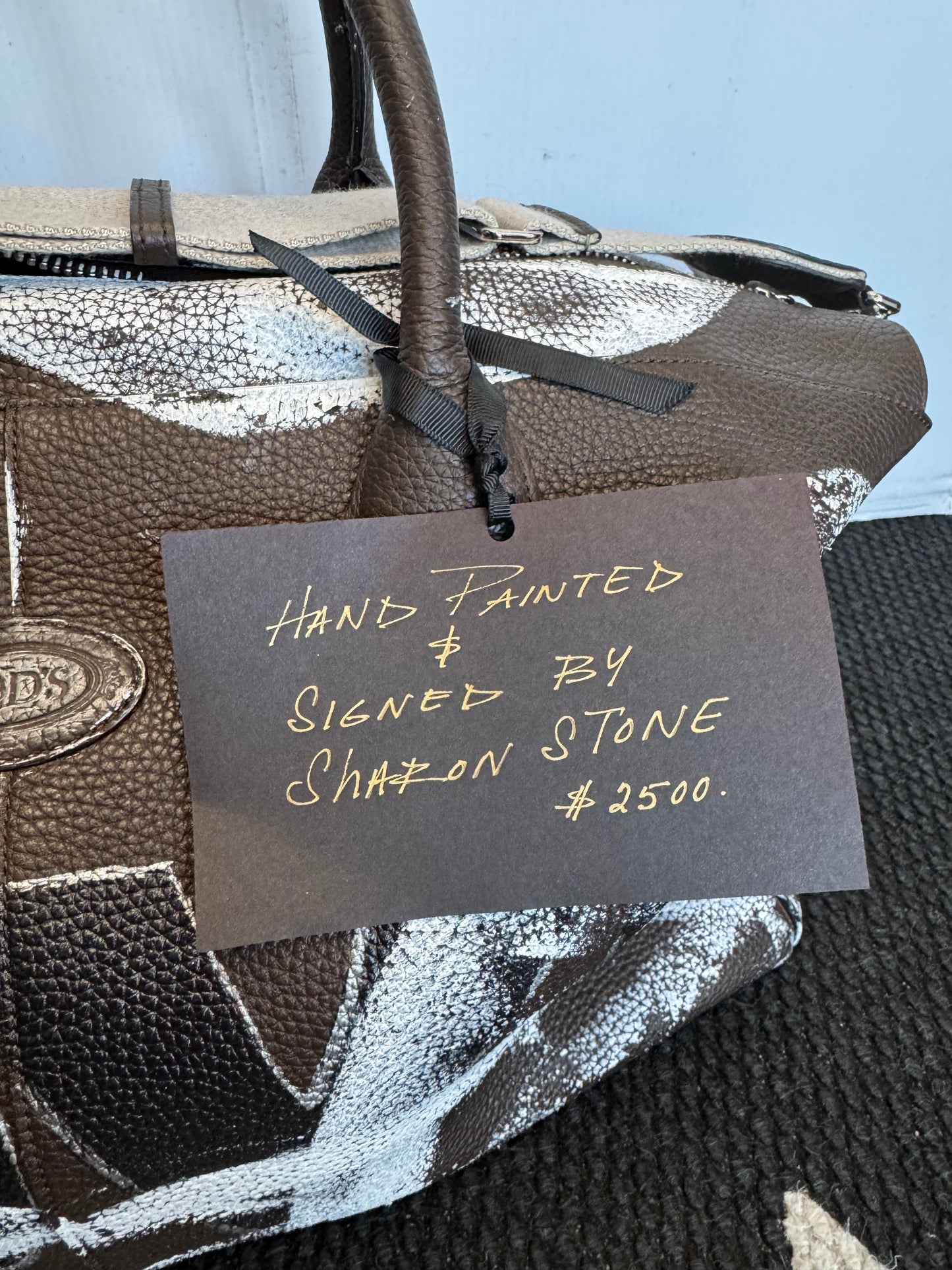 Hand-painted with "LOVE"and Signed by actress Sharon Stone this Tod's brown leather weekender looks as fab on the road as it does in your home a display housing cozy blankets.